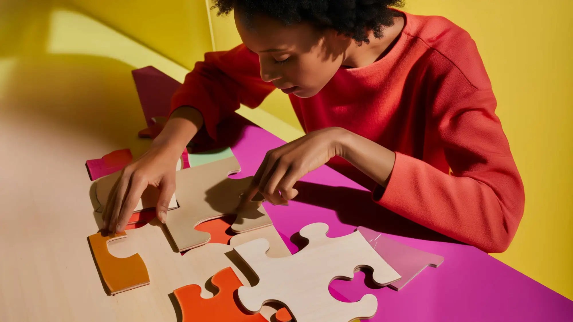 Una mujer con una camiseta de manga larga roja está ensamblando piezas de rompecabezas entrelazadas y coloridas en una superficie púrpura vibrante.